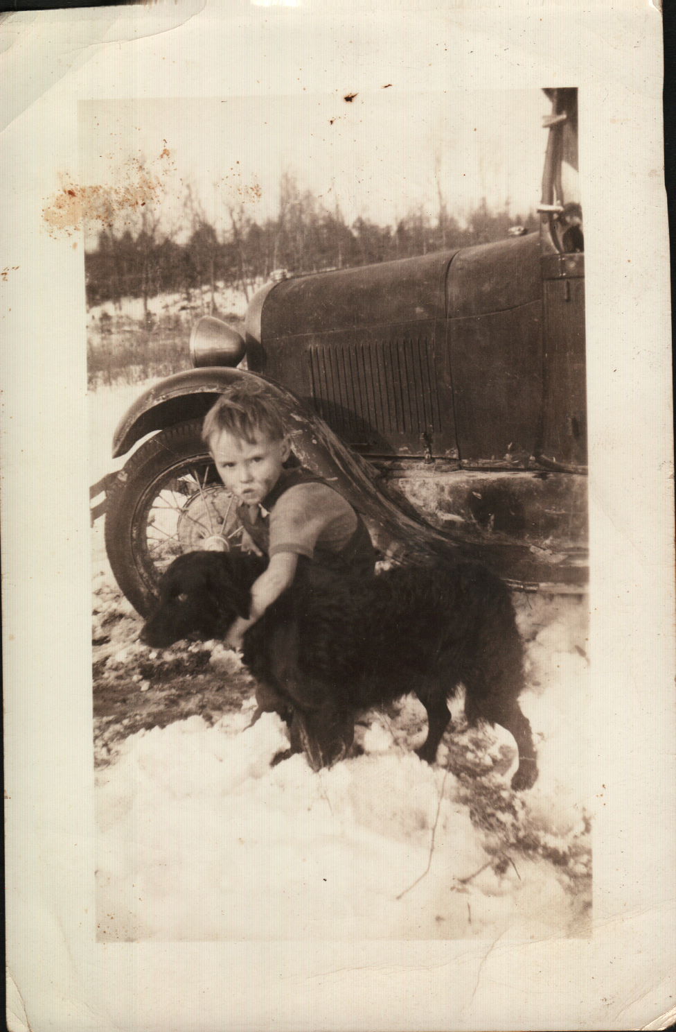 Vintage family photograph of a young boy with a dog beside an old vehicle